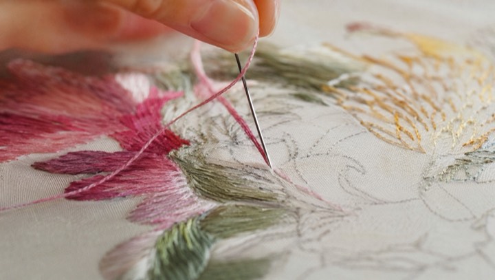 Close view of silk threads and a needle passing through embroidered fabric